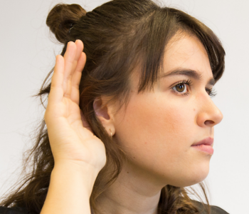 Eine Frau hört mit der Hand am Ohr