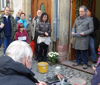 Eine Gruppe von Menschen macht eine Gedenkminute bei der Verlegung von neuen Stolpersteinen