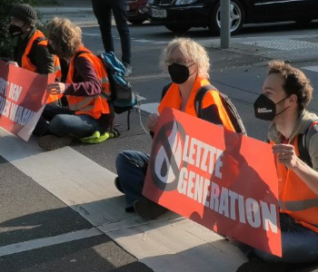 Das Foto zeigt eine Protestaktion der Letzten Generation in Heidelberg. Menschen sitzen auf der Straße. Sie blockieren die Straße.