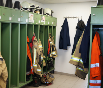 Auf dem Foto ist eine Umkleidekabine mit Feuerwehrkledung. Hier ziehen sich die Feuerwehrleute für den Einsatz um.